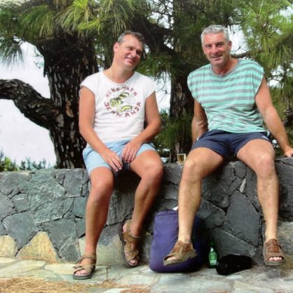 Bruno Pfister (rechts) mit seinem Partner Rolf Kundert in gesunden Zeiten auf einer Ferienreise. Sie sitzen in kurzen Hosen auf einer Steinmauer.