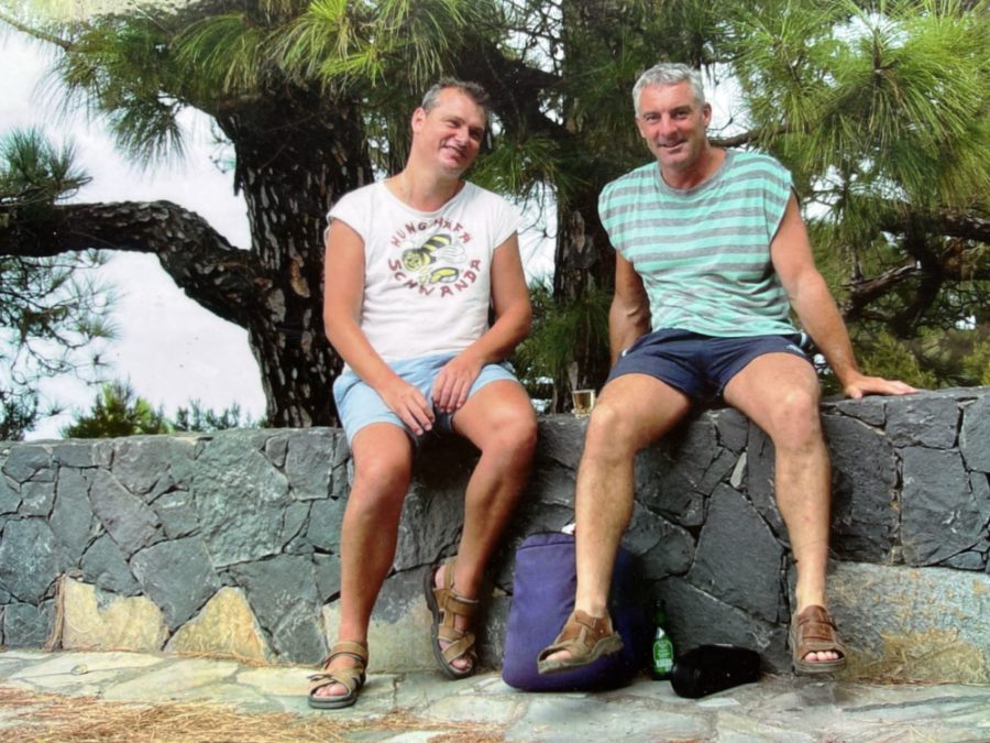 Bruno Pfister (rechts) mit seinem Partner Rolf Kundert in gesunden Zeiten auf einer Ferienreise. Sie sitzen in kurzen Hosen auf einer Steinmauer.