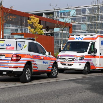 Ein Rettungswagen von Schutz & Rettung Zürich und ein Notarztfahrzeug stehen vor einer Wohnsiedlung.